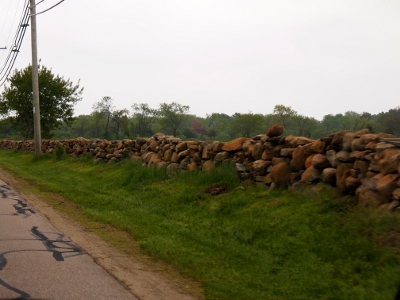 [Roughly stacked stones creating a wall along the roadside.]